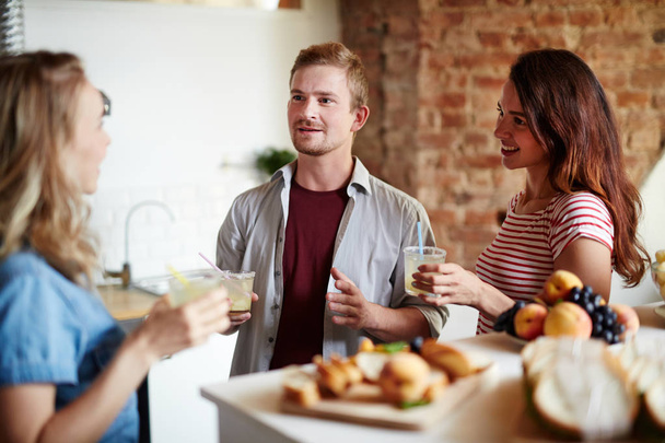 Two girls and guy with drinks having talk in the kitchen at home party - Photo, Image