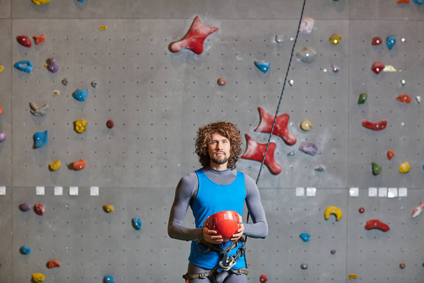 Active man in sportswear holding red protective helmet for indoor climbing - Foto, immagini