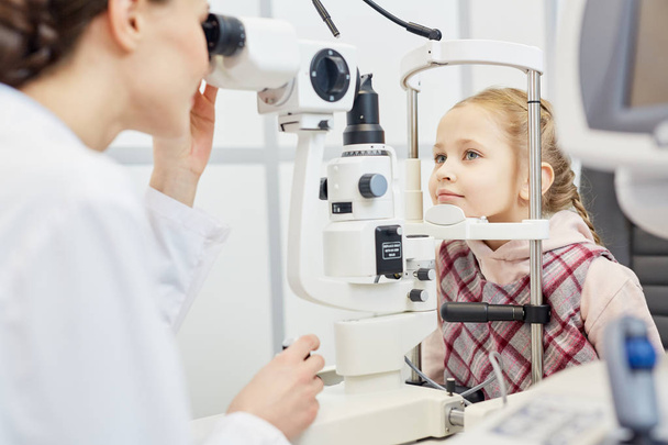 Young clinician checking eyesight of little girl on professional equipment - Zdjęcie, obraz