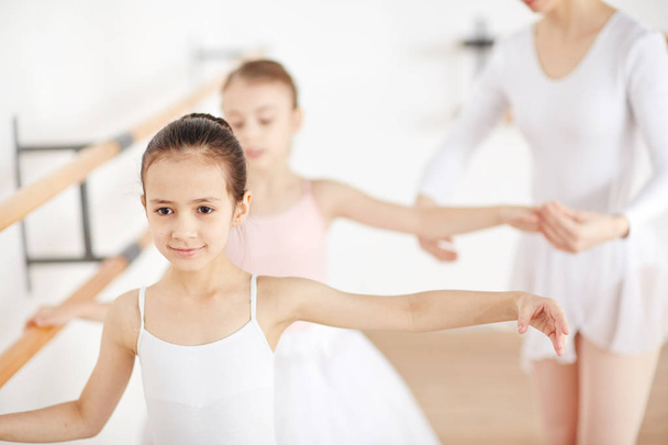 Привлекательные маленькие балерины, тренирующиеся в классе с помощью учителя
 - Фото, изображение