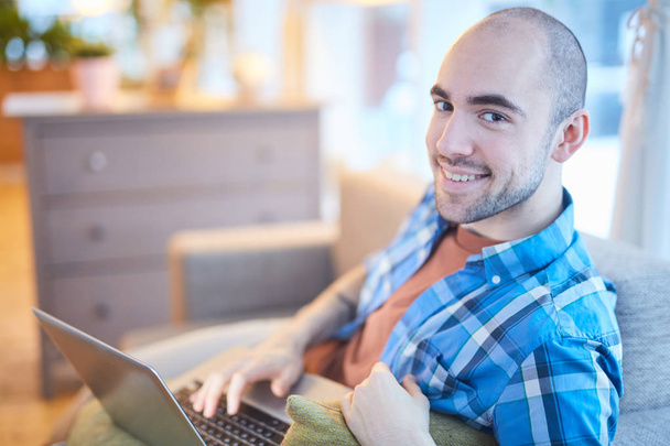 Молодий чоловік у повсякденному одязі відпочиває з ноутбуком під час пошуку в мережі або перегляду веб-трансляції
 - Фото, зображення