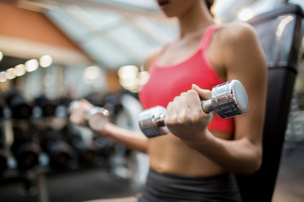 Midsection of sporty woman with dumbbells exercising in fitness club - Foto, immagini