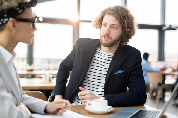 Jóvenes socios de negocios conversando sobre nuevos términos de joint venture mientras están sentados en la cafetería
 - Foto, imagen