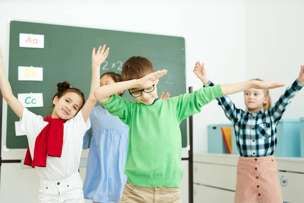 Niedliche Schulkinder in Freizeitkleidung tanzen nach dem Unterricht im Klassenzimmer und genießen die Pause - Foto, Bild