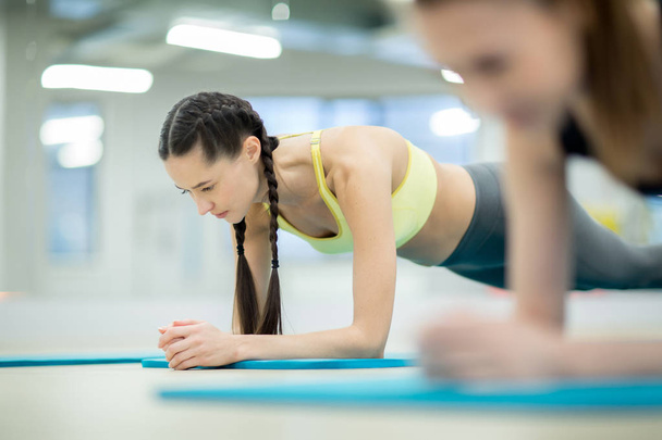 Jeunes femmes en vêtements de sport faisant des planches sur le sol tout en s'entraînant dans un centre de fitness
 - Photo, image
