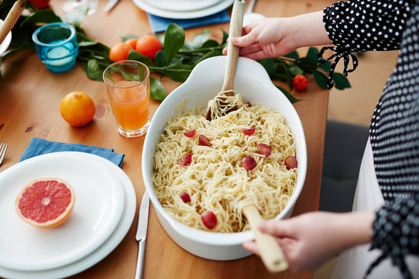 Lidské ruce s vařečky míchání vařené špagety s vegs porcelán pánvi před podáváním - Fotografie, Obrázek