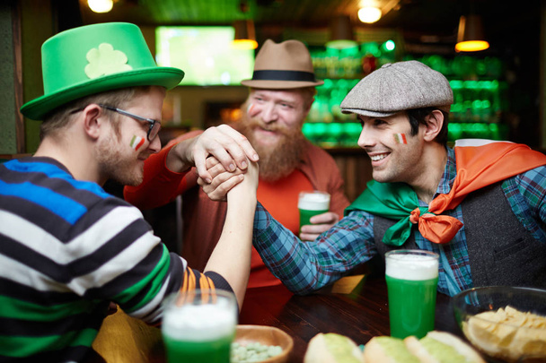 Two irish men armwrestling on table while spending time in pub on Saint Patrick day - Photo, Image