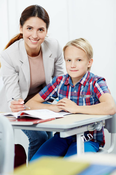 Adorable boy and his teacher looking at camera with smiles while working over new material - Φωτογραφία, εικόνα