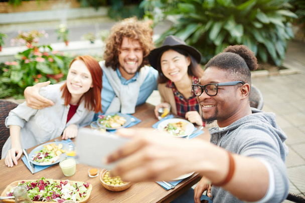 Ragazzo afro-americano con smartphone che fa selfie di lui e dei suoi amici durante la cena festiva in giardino
 - Foto, immagini