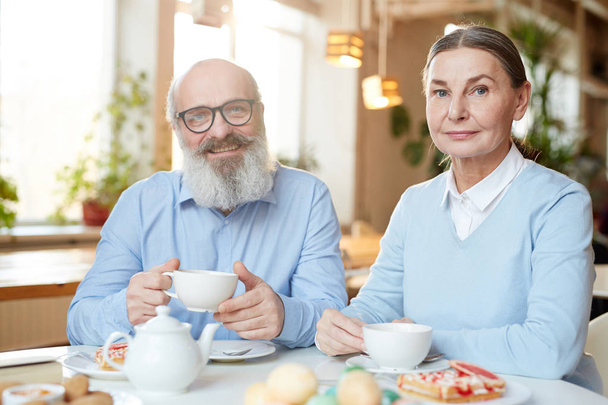 Счастливый зрелый мужчина и женщина смотрят в камеру, проводя время в кафе к десерту
 - Фото, изображение