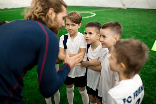 Joven entrenador de fútbol hablando con el equipo de pequeños jugadores en el campo durante el descanso entre los juegos
 - Foto, Imagen