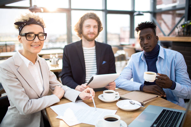 Jeune femme d'affaires et deux hommes assis à table dans un café, prenant un café et travaillant sur un nouveau projet
 - Photo, image