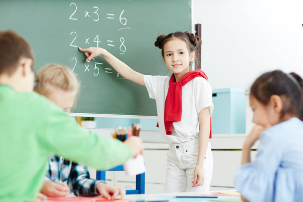 Slim meisje permanent gebruik gemaakt van blackboard en wijzend op een van de bedragen tijdens de les van wiskunde - Foto, afbeelding