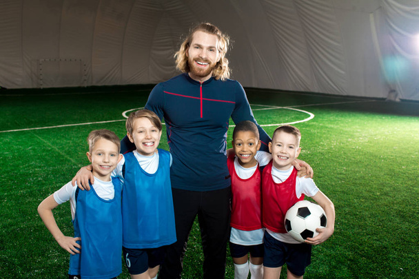 Successful football trainer and four happy boys in uniform standing on green soccer field - Foto, Imagen