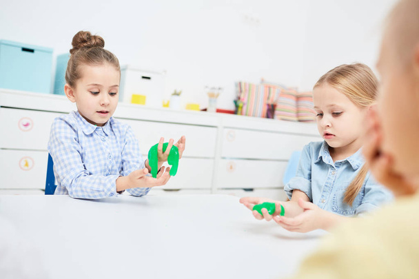 Little girls playing with green slime in kindergarten over table - Zdjęcie, obraz