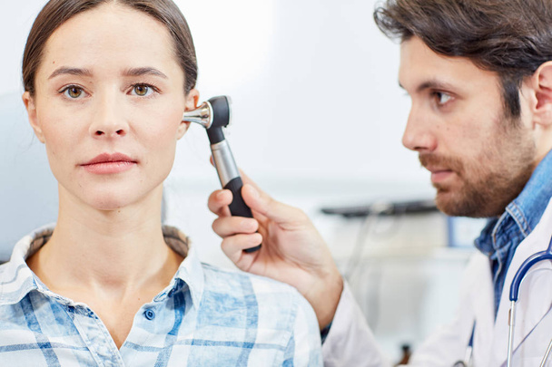 Young professional doctor examining ears of female patient in clinics - Photo, Image