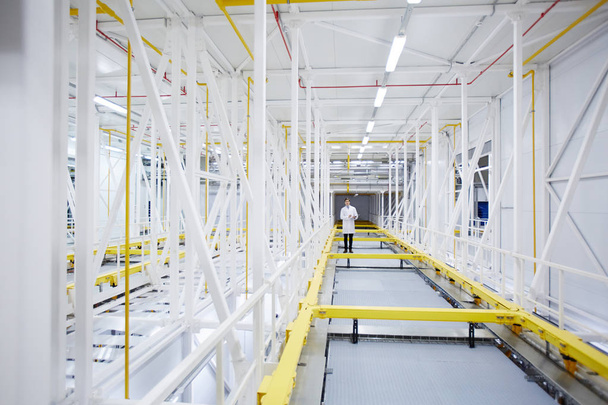 Long aisle in modern mining farm with young engineer standing in the middle of it - Photo, Image