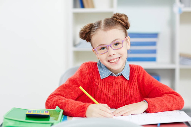 Cute schoolgirl with yellow crayon drawing at lesson by her desk - Photo, Image