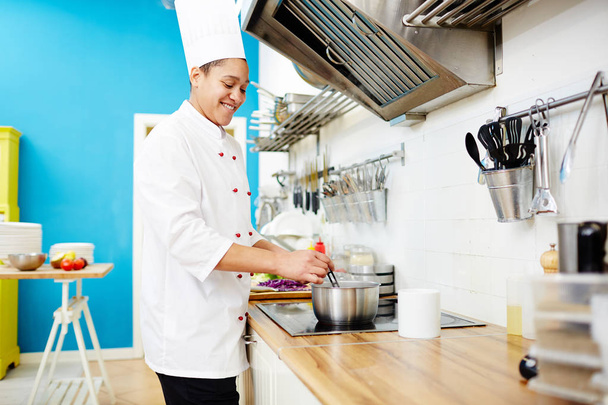 Счастливый молодой шеф-повар смешивает ингредиенты кипящей пищи в стальной сковороде на кухне
 - Фото, изображение