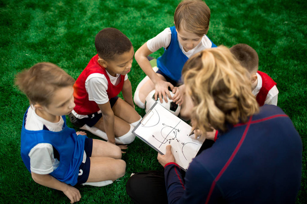 Football instructor drawing scheme of moving during soccer game or training and explaining it to group of boys - Photo, Image