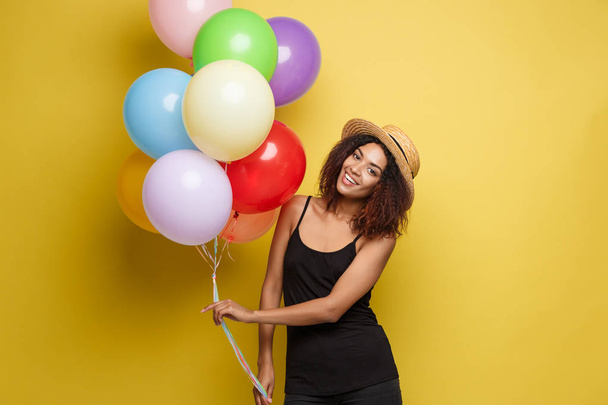 Concepto de celebración - Primer plano Retrato feliz joven hermosa mujer africana en camiseta negra sonriendo con globo de fiesta de colores. Fondo de estudio Pastel amarillo
 - Foto, imagen