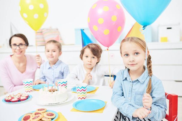 Lindo niño con globo rosa, sus amigos y maestro reunidos por la mesa festiva en la fiesta de cumpleaños
 - Foto, imagen