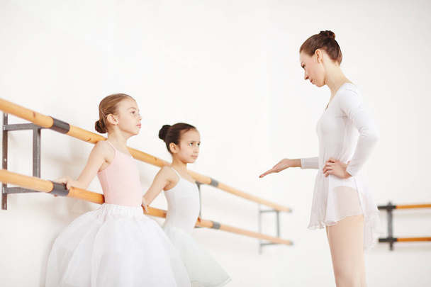 Ammattimainen baletinopettaja puhuu yhdelle pienistä ballerinoista luokkahuoneessa harjoittelun aikana
 - Valokuva, kuva