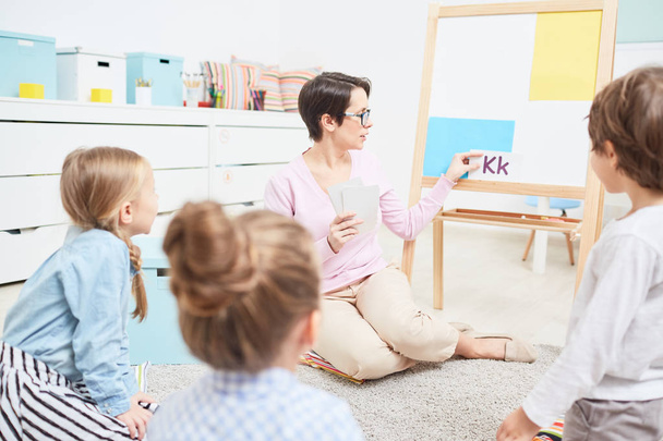 Professora jovem mostrando e contando sobre K carta no quadro branco na lição no jardim de infância
 - Foto, Imagem