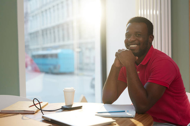 Afro-amerikai menedzser toothy mosoly ül az asztal munkanap folyamán - Fotó, kép