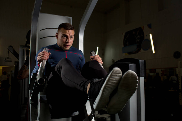 Young man making effort during difficult exercise for arms on sports equipment in gym - Foto, afbeelding