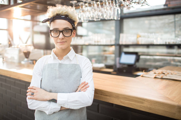 Young waitress in eyeglasses and apron crossing her arms on chest and looking at camera - Photo, Image