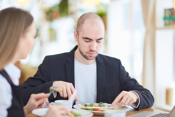 Businessman eating vegetable salad in restaurant during lunch break and talking to colleague - Foto, Imagem