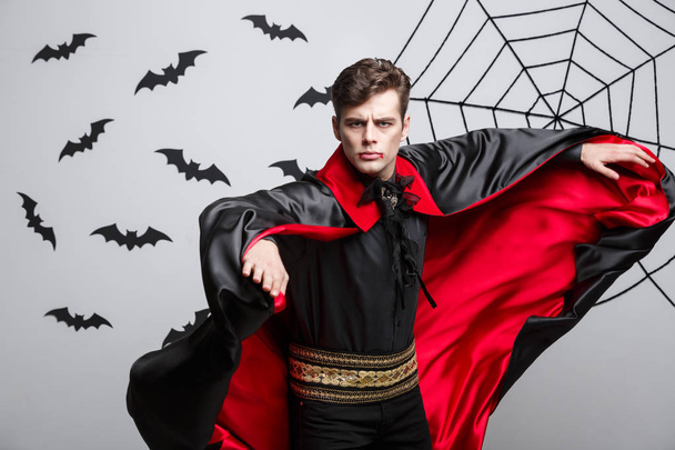 Хэллоуин вампиров - Портрет красавца-кавказца в костюме вампира на Хэллоуин в красном и черном плаще
. - Фото, изображение