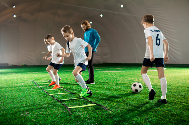 Niños jóvenes en uniforme haciendo ejercicio durante el entrenamiento de fútbol en el césped verde
 - Foto, Imagen
