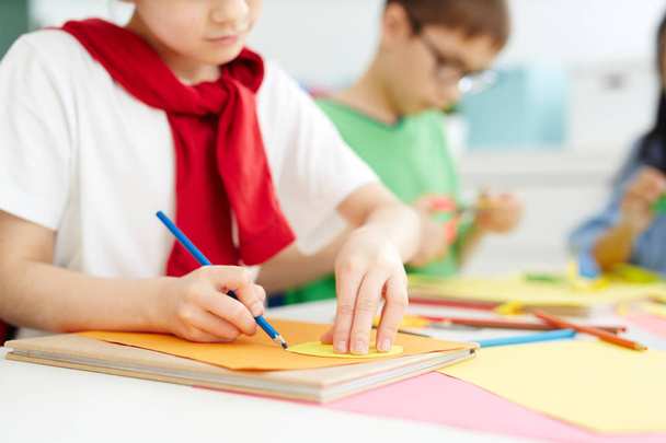 Schoolgirl outlining paper workpiece on other sheet of paper with blue crayon - Fotografie, Obrázek