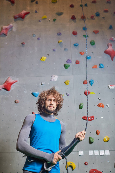 Atraktivní mladý muž s kudrnatými vlasy drží lano na lezení před tréninkem - Fotografie, Obrázek