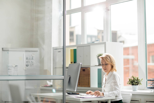 Trabalhadora de escritório séria que se concentra na leitura de documentos pelo seu local de trabalho
 - Foto, Imagem