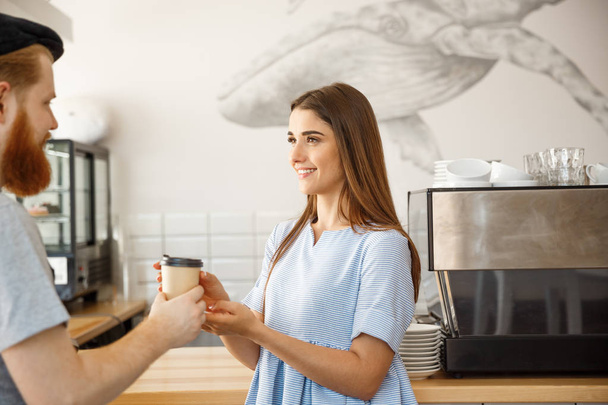 Coffee Business Concept - il giovane barbuto intelligente si diverte a parlare e regalare una tazza di caffè da asporto a un cliente carino
. - Foto, immagini