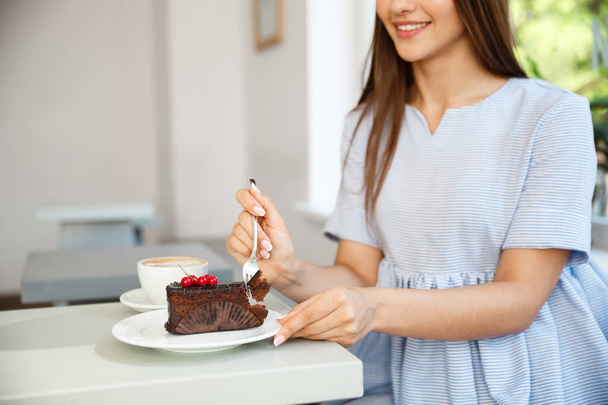 Joven atractiva dama caucásica disfrutar de comer pastel de chocolate con café caliente en la cafetería moderna al mediodía
. - Foto, imagen