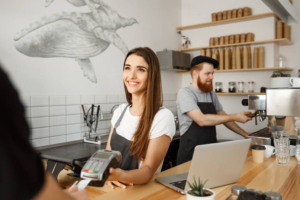 Coffee Business Concept - Hermosa barista femenina dando servicio de pago para el cliente con tarjeta de crédito y sonriendo mientras trabaja en el mostrador del bar en la cafetería moderna
. - Foto, imagen