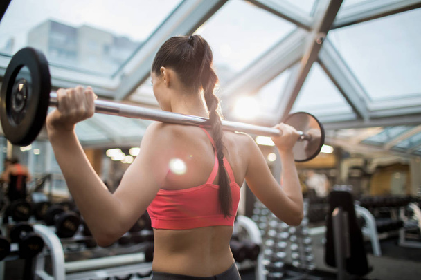 Vista trasera de una joven fuerte levantando pesadas pesas durante el entrenamiento en el gimnasio
 - Foto, imagen