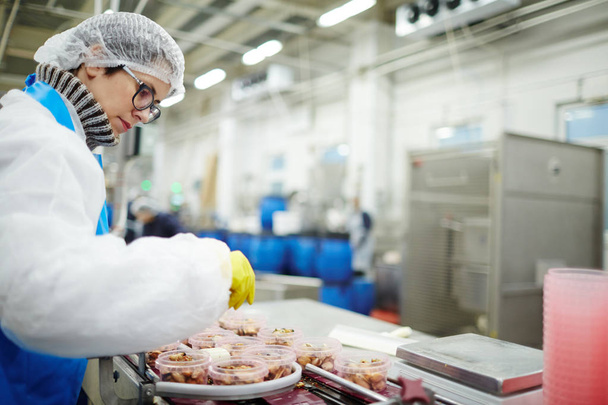 Young staff sorting seafood into plastic containers while standing by processing line in factory - Photo, Image