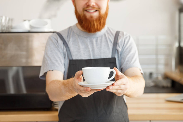Właściciel firmy kawa koncepcja - portret szczęśliwy młody Brodaty kaukaski barista w fartuch z pewnie właśnie serwis gorącej kawy do klienta w kawiarni licznika. - Zdjęcie, obraz