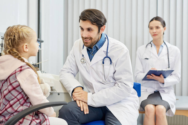 Sorridente giovane clinico ascoltando piccole lamentele dei pazienti mentre il suo assistente prende appunti
 - Foto, immagini