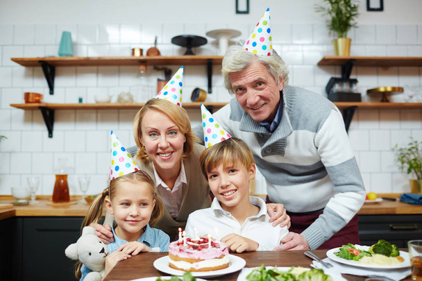 Urocze dzieci i ich dziadków w urodziny czapki siedzi przez świąteczny stół - Zdjęcie, obraz