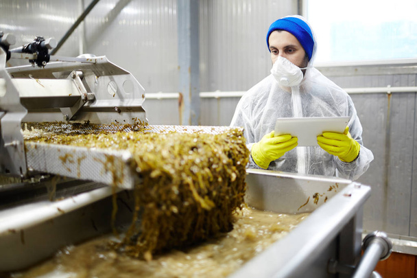 Молодой работник завода по переработке морепродуктов, контролирующий процесс приготовления салата из водорослей
 - Фото, изображение