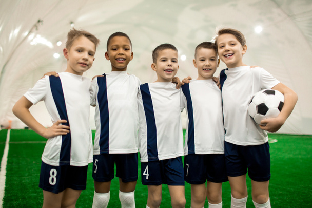 Team van jonge succesvolle voetballers in uniforme staande in rij op veld - Foto, afbeelding