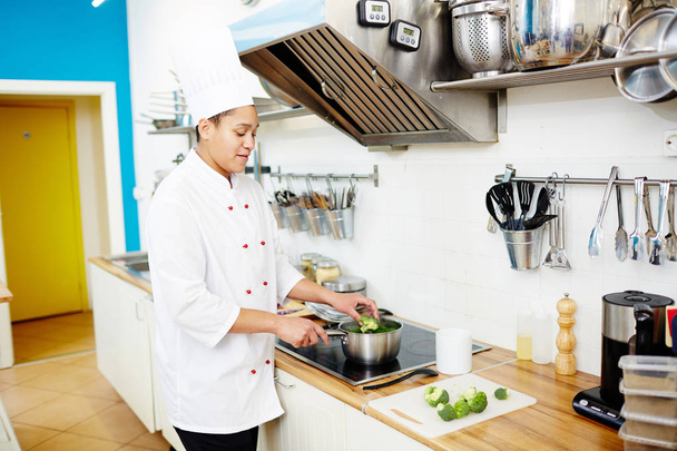 Młody kucharz kobiece umieszczenie elementów brokuły do miski z wodą, zagotować - Zdjęcie, obraz