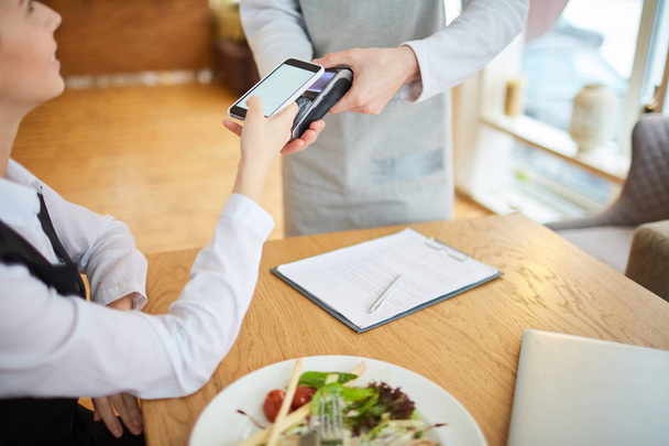 Jovem cliente do sexo feminino pagando por comida através de seu smartphone no café
 - Foto, Imagem