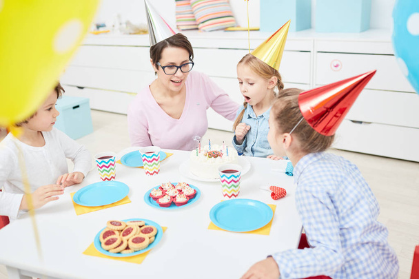 Kislány fújt gyertyákat születésnapi torta neki között a groupmates és a tanár az óvodában - Fotó, kép